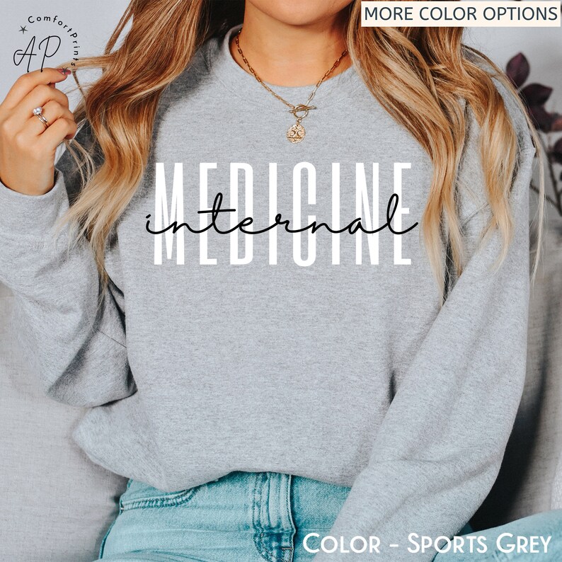 May include: A gray sweatshirt with the text "internal medicine" printed in white on the front. The sweatshirt is being worn by a person with long blonde hair. The text "COLOR - SPORTS GREY" is printed at the bottom of the image.