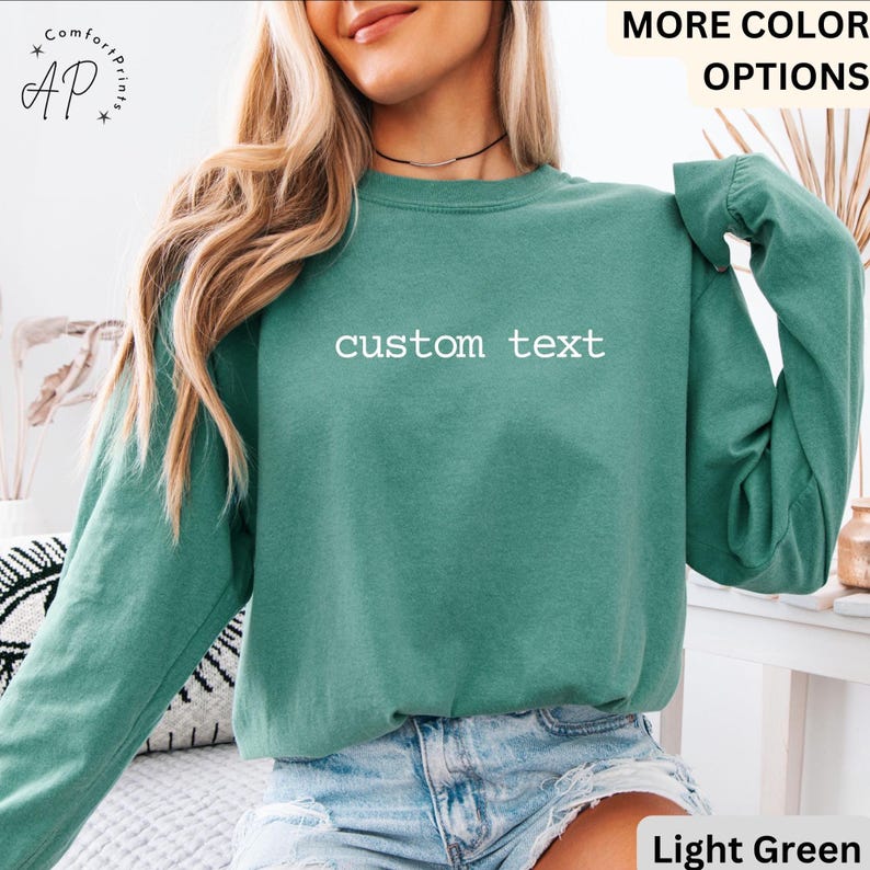 May include: A light green sweatshirt with the words "custom text" in white. The long-sleeved shirt is a solid color and is made of a soft material. The shirt is a comfortable, casual style.