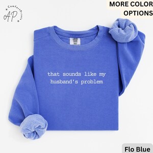 May include: Flo Blue sweatshirt with the text "that sounds like my husband's problem" in white. The sweatshirt has a crew neck and long sleeves with cuffed ends. The Comfort Colors label is visible.