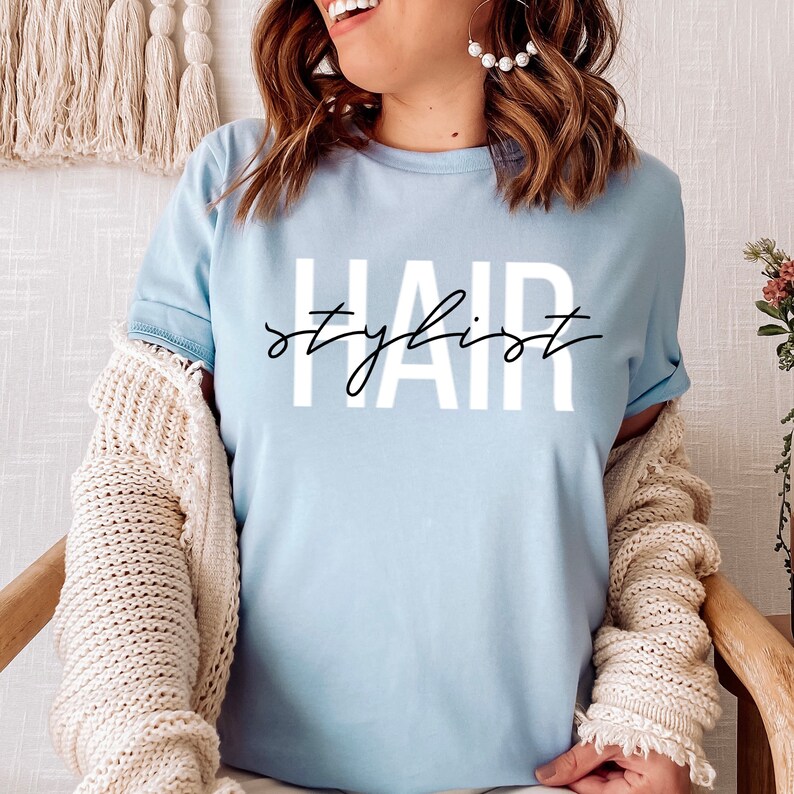 K&ouml;nnte beinhalten: Ein hellblaues T-Shirt mit dem Aufdruck "Hair stylist" in Wei&szlig; auf der Vorderseite.