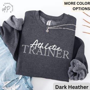 Könnte beinhalten: Dunkelgrauer Sweatshirt mit dem Text "Athletic TRAINER" in weißer Schrift.