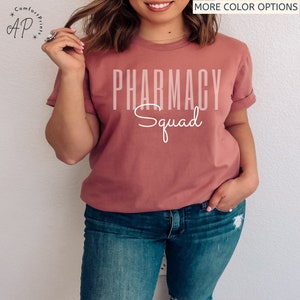 May include: A mauve t-shirt with the text "Pharmacy Squad" in white lettering.
