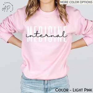 May include: A light pink sweatshirt with the text "INTERNAL MEDICINE" printed in white on the front.