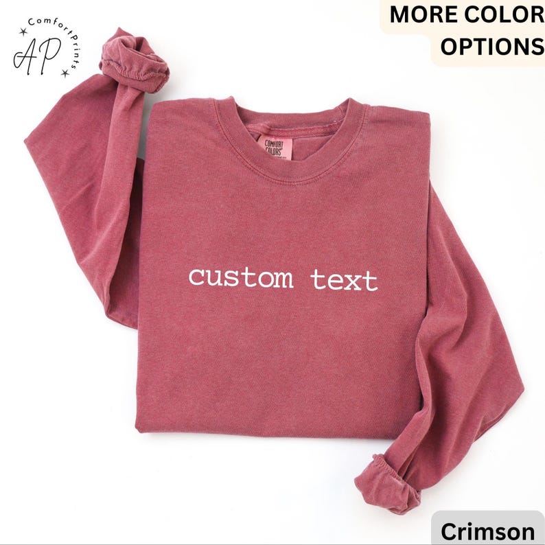 May include: Crimson long-sleeve shirt with the text "custom text" in white. The shirt has a crew neck and rolled-up sleeves. The shirt is a solid color and is made of a soft material. The shirt is a comfortable, casual style.