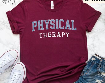 May include: Maroon t-shirt with the words "PHYSICAL THERAPY" in a blue and white collegiate font. The shirt is displayed with white sneakers and denim shorts. The words "MORE COLOR OPTIONS" are at the top.