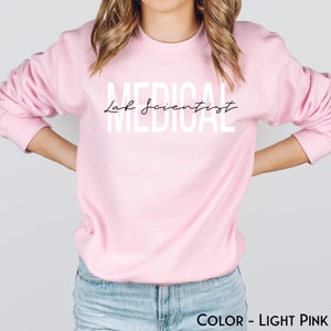 May include: A light pink sweatshirt with the text "Medical Lab Scientist" in white letters.