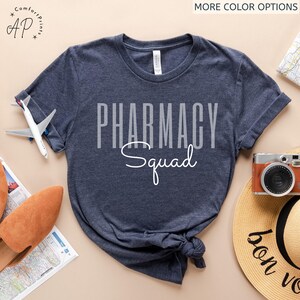 May include: A navy blue t-shirt with the text "Pharmacy Squad" in white lettering. The text is in a bold, blocky font with the word "Squad" in a cursive script.