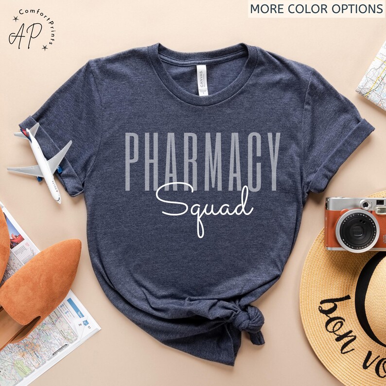 May include: A navy blue t-shirt with the text "Pharmacy Squad" in white lettering. The text is in a bold, blocky font with the word "Squad" in a cursive script.