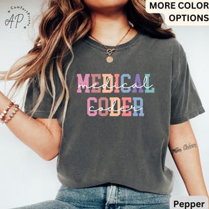 May include: A grey t-shirt with the text "MEDICAL CODER" in rainbow colours. The text is in a playful, handwritten font.
