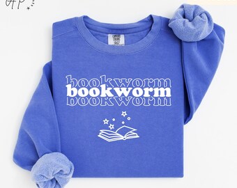 May include: A blue sweatshirt with the text "bookworm" repeated three times in a retro font. A white outline of a book with stars above it is centered below the text.