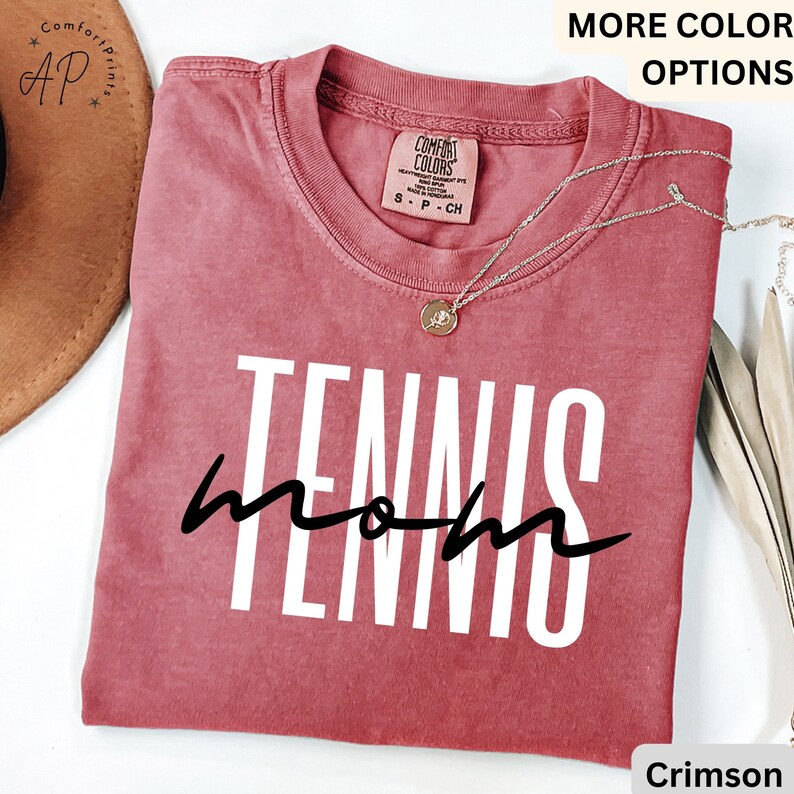 May include: Crimson red t-shirt with the text "Tennis Mom" in white letters. The shirt is made of a soft, comfortable material.