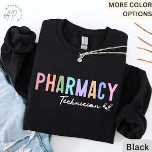 Peut inclure: Sweat-shirt noir avec le texte "PHARMACY Technician" en couleurs arc-en-ciel et deux icônes de pilules.