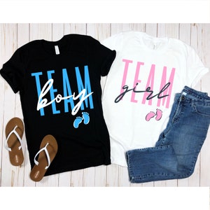 May include: Two t-shirts, one black and one white, with the text "TEAM boy" and "TEAM girl" in white and pink lettering. Each shirt has a pair of baby footprints, one blue and one pink.