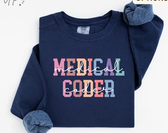 May include: A navy blue crewneck sweatshirt featuring the text "MEDICAL CODER" in a multi-colored block font with a white cursive script overlay. The garment has long sleeves with ribbed cuffs and a Comfort Colors brand label at the neckline.