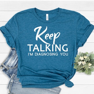 May include: A teal blue t-shirt with white text that reads "Keep Talking I'm Diagnosing You".