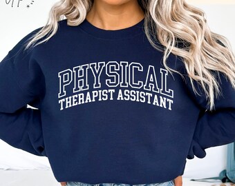 Op de afbeelding: Donkerblauwe trui met de tekst "PHYSICAL THERAPIST ASSISTANT" in witte omrande letters.