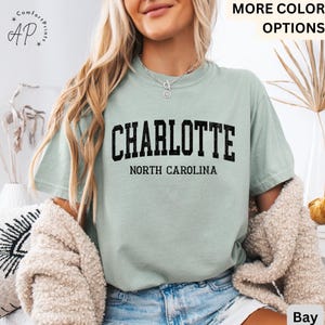Op de afbeelding: Lichtgroen t-shirt met het woord "CHARLOTTE" in zwarte blokletters boven "NORTH CAROLINA". Het shirt is gemaakt van een zacht, comfortabel materiaal.
