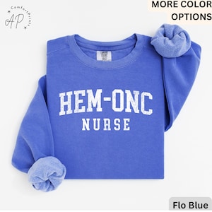 Peut inclure: Un sweat-shirt bleu avec le texte "HEM-ONC NURSE" en lettres blanches vieillies.