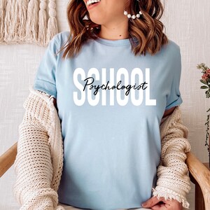 Op de afbeelding: Een lichtblauw T-shirt met de tekst "School Psychologist" gedrukt in witte letters.
