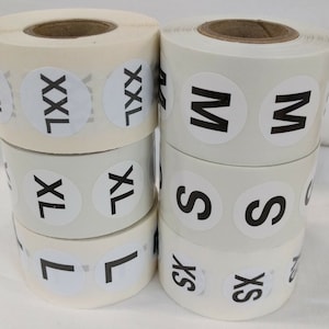 May include: Four rolls of white sticker labels with black text. The labels are in different sizes, with the text "XXL", "XL", "L", "M", "S", and "XS".