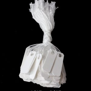 May include: A bundle of white rectangular tags with a hole at the top, tied together with white string. The tags measure 1/4" x 3/4". The text "1/4" x 3/4"" is displayed at the bottom of the image.