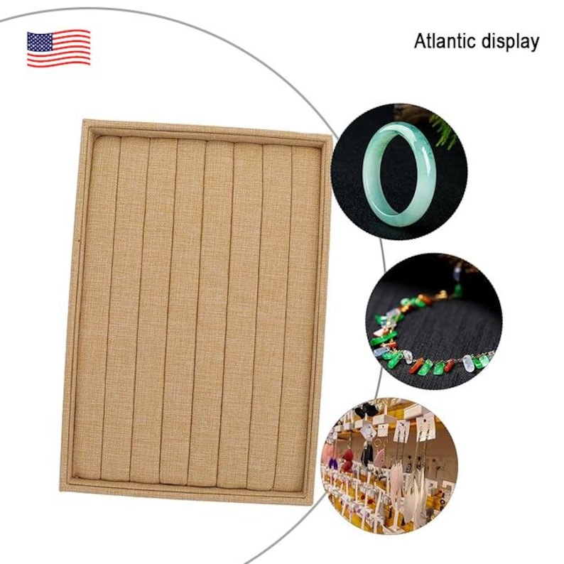 May include: A beige fabric ring display tray with 12 slots for storing rings. The tray is made of a soft, textured fabric and has a rectangular shape. The tray is shown in front of a white background with a small American flag in the top left corner. The text "Atlantic display" is in the top right corner of the image.