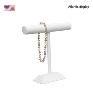May include: White jewelry display stand with a T-shaped base and a round top. A pearl necklace is displayed on the stand.