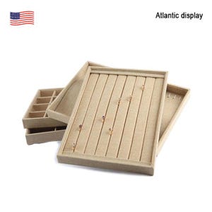 May include: A beige jewelry display tray with multiple compartments for rings and earrings. The tray is made of a soft, textured fabric and has a simple, elegant design.