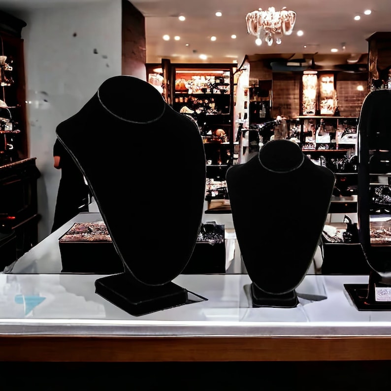 May include: Three black velvet necklace display stands on a white countertop. The stands are different sizes and are all empty.