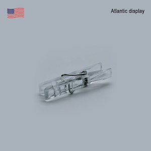 May include: A clear plastic clothespin with a metal spring. The clothespin is designed for hanging items.