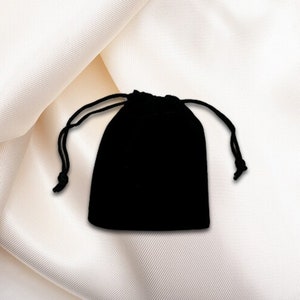 May include: A small black velvet drawstring bag. The bag is closed and lying on a white fabric surface.