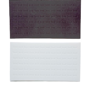 May include: Two rectangular jewellery display inserts. One is dark grey, the other is white. Both have rows of small, evenly spaced slots designed to hold rings or other small jewellery items. The inserts are likely made of foam or a similar material.