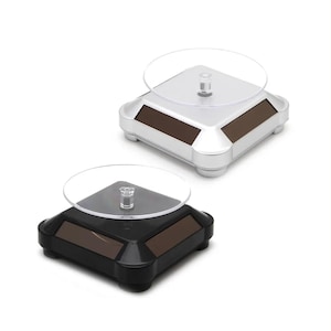 May include: Two solar-powered display stands. One is silver with brown panels, the other is black with brown panels. Each has a clear, circular top and a square base with rounded corners and small feet.