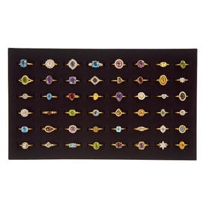 May include: A display of gold rings with diverse gemstone designs, including round, oval, and pear cuts. The gemstones are in various colours, such as blue, green, purple, and yellow. The rings are presented on a black surface.