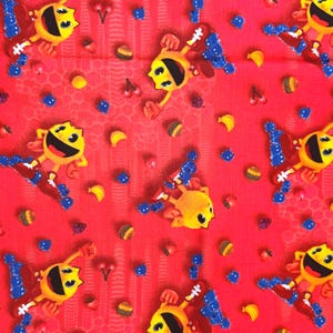 Pode incluir: Um tecido vermelho com um padrão repetitivo de personagens Pac-Man amarelos usando tênis azuis e brancos, intercalados com pequenos ícones de cerejas, bananas, hambúrgueres e formas azuis semelhantes a fantasmas em toda a superfície.