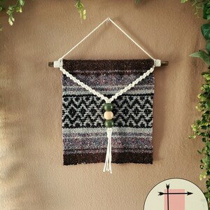 May include: A woven wall hanging with a brown, black, and white geometric pattern. The hanging has a white tassel and a string of wooden and green beads.