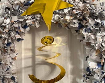 May include: A gold star and a gold spiral hanging from a wreath made of white fabric scraps with black and blue accents.
