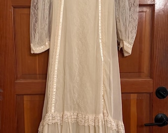 May include: Ivory vintage wedding dress with long, sheer lace sleeves. The dress features a high neckline, decorative buttons, and lace trim. The skirt has a layered, flowing design, creating a romantic and ethereal look.