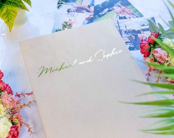 May include: A beige photo album with the text "Michael and Sophie" in silver lettering on the front cover.
