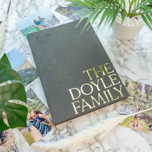May include: A dark grey photo album with gold lettering that reads "The Doyle Family". The album is surrounded by photos of a family on holiday.