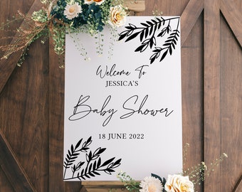 May include: White welcome sign with black floral designs and the text "Welcome to Jessica's Baby Shower 18 June 2022".