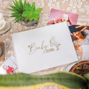 Puede incluir: Diario blanco para beb&eacute; con una ilustraci&oacute;n de cig&uuml;e&ntilde;a dorada y el texto "My Baby Journal".