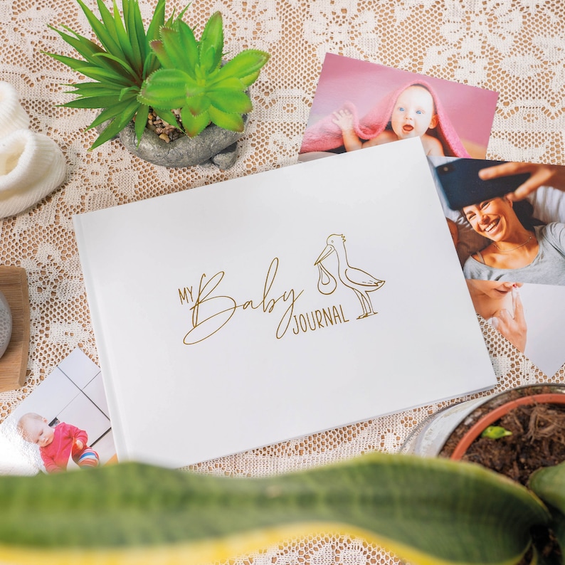 Puede incluir: Diario blanco para beb&eacute; con una ilustraci&oacute;n de cig&uuml;e&ntilde;a dorada y el texto "My Baby Journal".