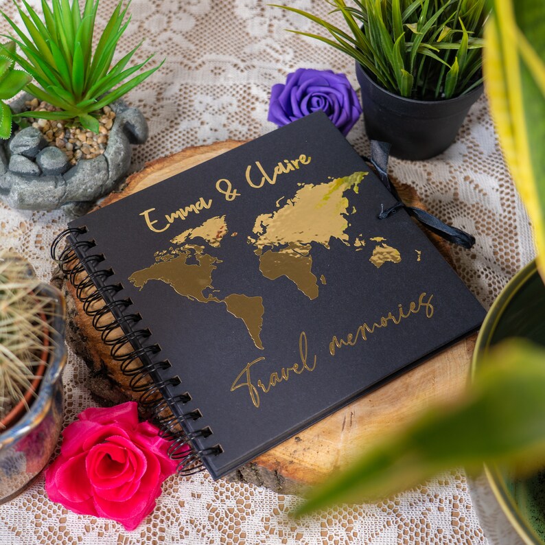 Peut inclure: Journal de voyage noir avec une carte du monde en feuille d'or et le texte "Emma & Claire Travel Memories" sur la couverture.