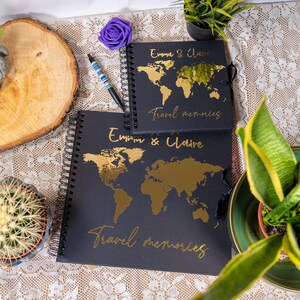Peut inclure: Deux carnets &agrave; spirales noirs avec des accents dor&eacute;s. Les couvertures pr&eacute;sentent une carte du monde et le texte "Emma & Claire Travel Memories".