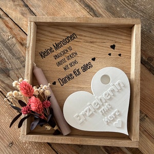 May include: A wooden box with a white heart-shaped plaque that says "Erzieherin mit Herz" (Teacher with heart). The box also has a small bouquet of dried flowers and a white candle. The text on the box reads "Kleine Menschen brauchen so grosse Herzen wie deins. Danke f&uuml;r alles" (Small people need such big hearts like yours. Thank you for everything).