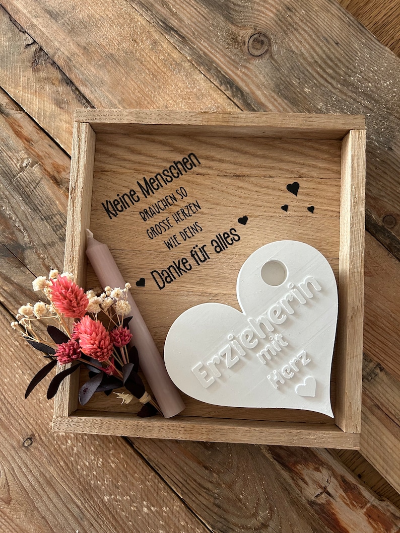 May include: A wooden box with a white heart-shaped plaque that says "Erzieherin mit Herz" (Teacher with heart). The box also has a small bouquet of dried flowers and a white candle. The text on the box reads "Kleine Menschen brauchen so grosse Herzen wie deins. Danke f&uuml;r alles" (Small people need such big hearts like yours. Thank you for everything).