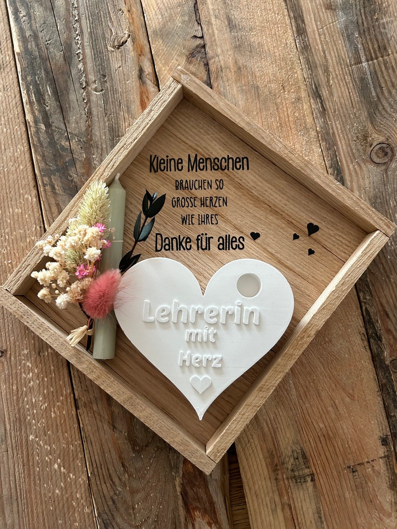 May include: A wooden tray with a white heart-shaped plaque that says "Lehrerin mit Herz" (Teacher with Heart). The tray also has a small bouquet of dried flowers and a white candle.