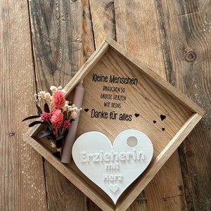 May include: A white wooden heart-shaped plaque with the text "Erzieherin mit Herz" on a wooden tray with a small bouquet of dried flowers and a candle. The tray also has the text "Kleine Menschen brauchen so grosse Herzen wie deins Danke f&uuml;r alles" on it.