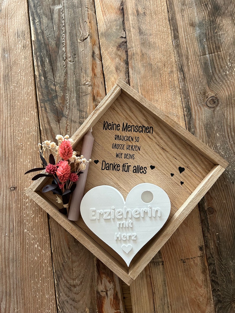 May include: A white wooden heart-shaped plaque with the text "Erzieherin mit Herz" on a wooden tray with a small bouquet of dried flowers and a candle. The tray also has the text "Kleine Menschen brauchen so grosse Herzen wie deins Danke f&uuml;r alles" on it.